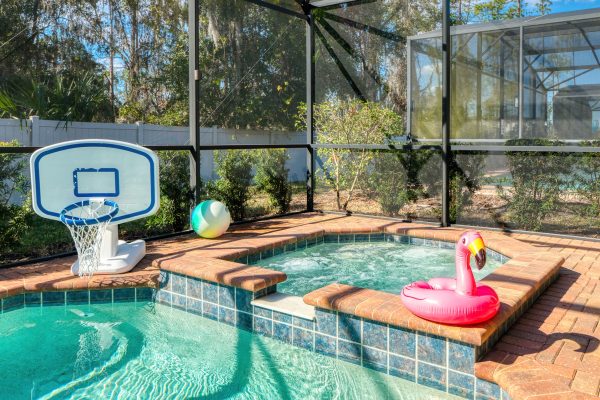 Private pool with basketball hoop and pink flamingo float in screened enclosure at Magic Moments Kissimmee vacation villa